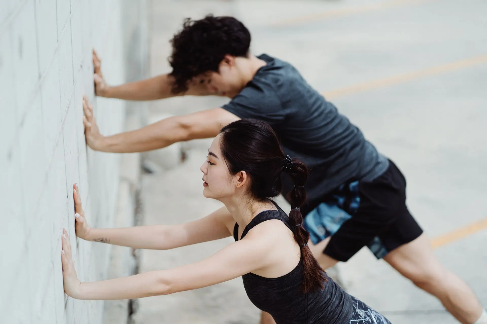 Two adults exercising and stretching against an outdoor urban wall, focusing on fitness and well-being.