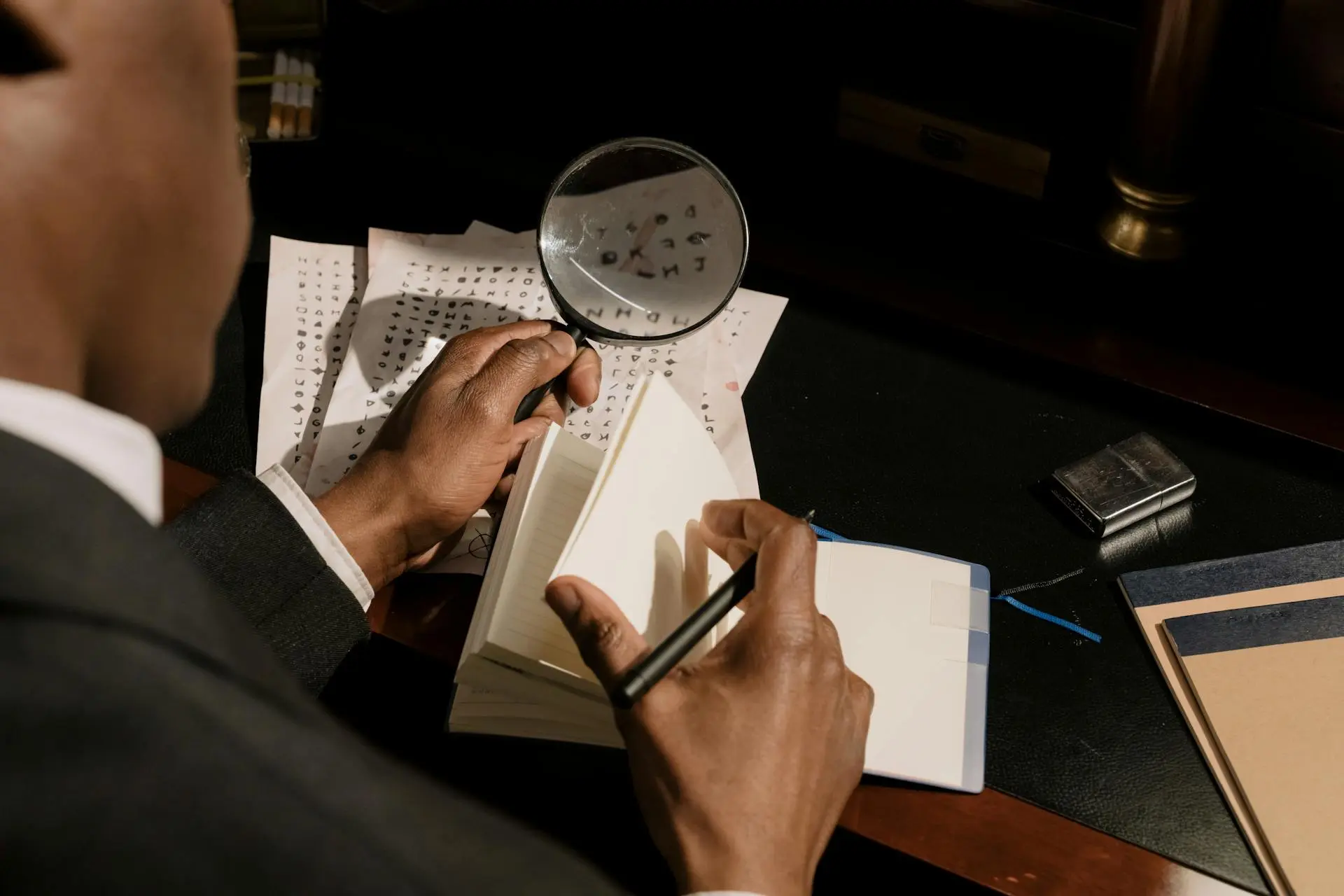 Man seated at a desk holding a magnifying glass in one hand and deciphering symbols on individual pieces of paper